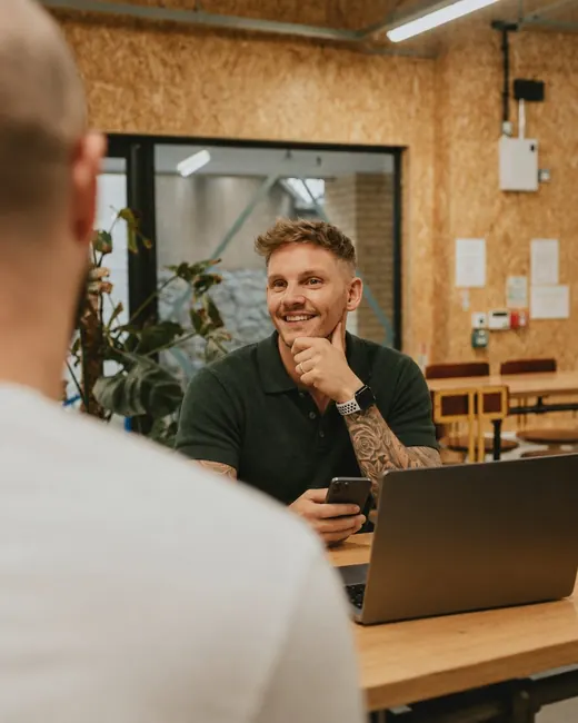 Homem de 35 anos sorrindo com o celular num espaço de coworking